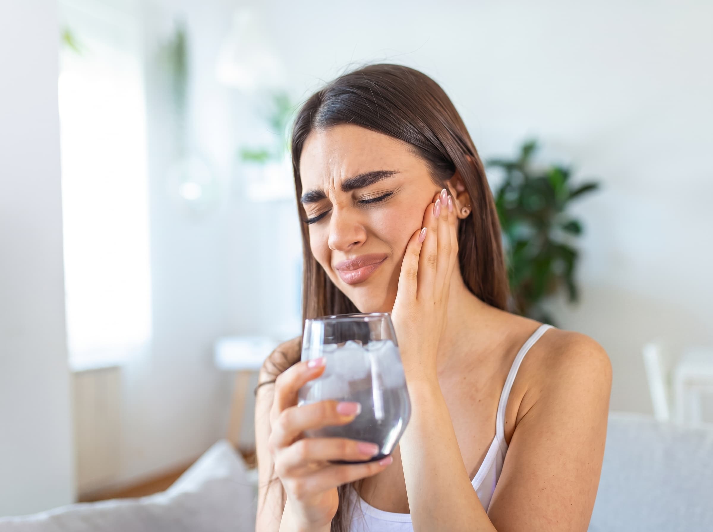 Donna con un bicchiere di acqua ghiacciata porta la mano alla guancia per una fitta ai denti