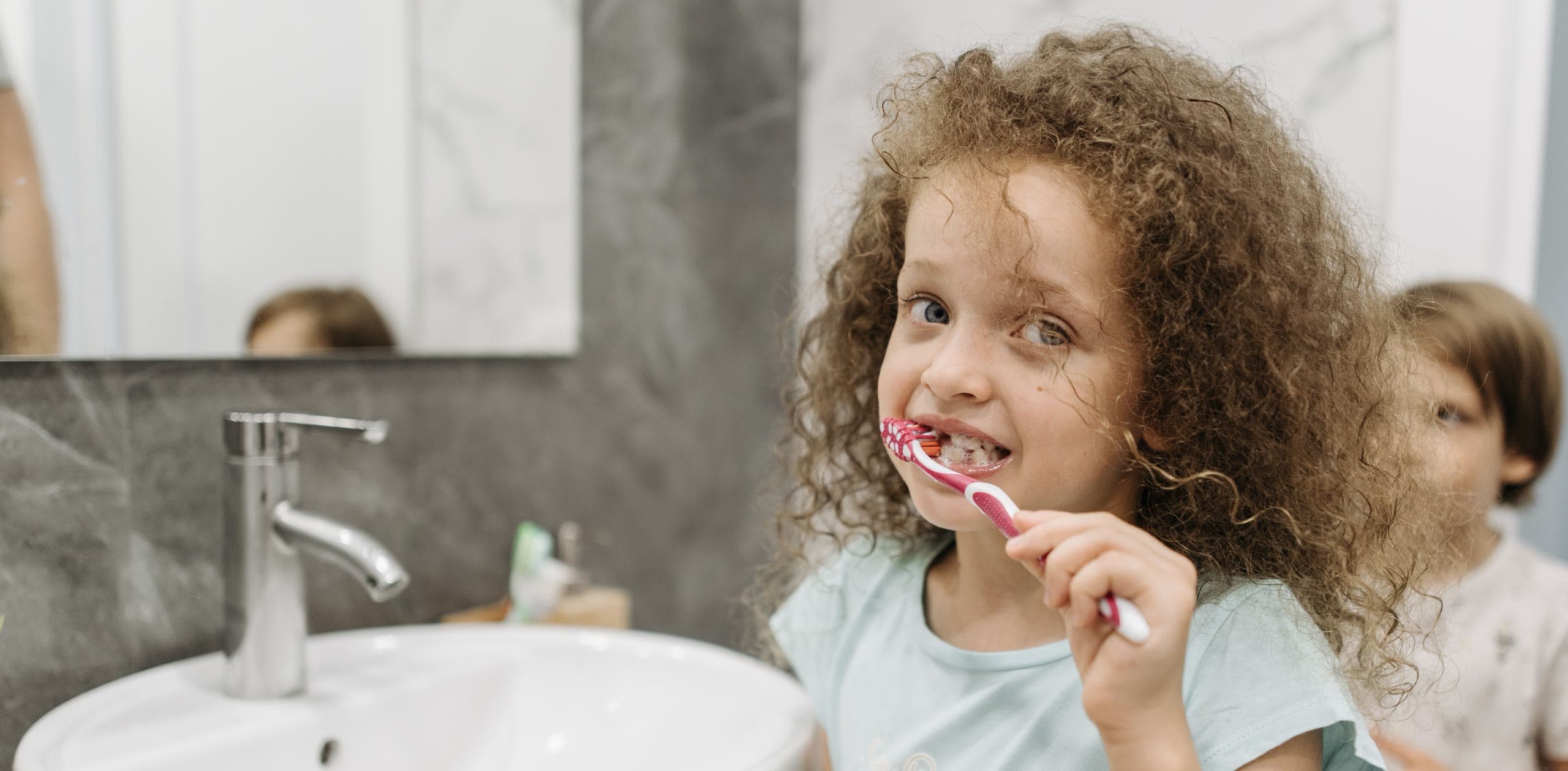 Bambina si lava i denti con lo spazzolino davanti allo specchio del bagno